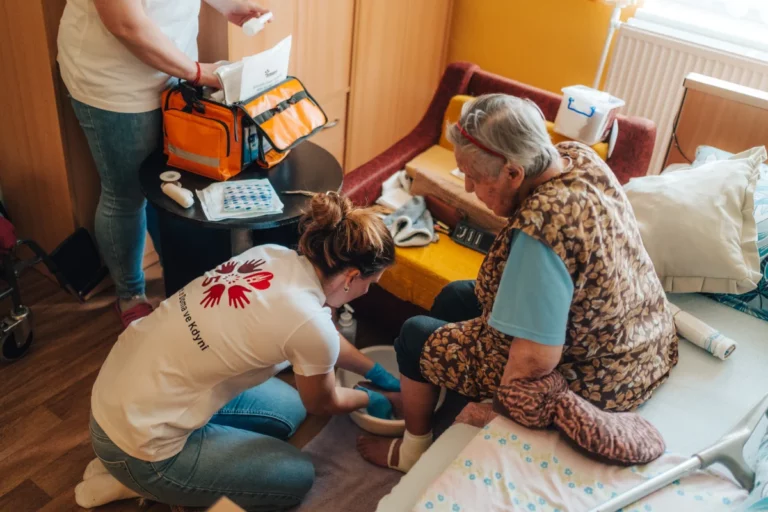 Zdravotní sestřička Doma ve Kdyni sedí v křesle a připravuje zdravotnické pomůcky, fotografie je vložená do tvaru dílku puzzle.